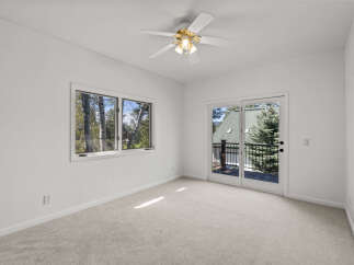 This bright and airy bedroom features a large window offering scenic views of lush trees and a private balcony accessible through glass double doors.