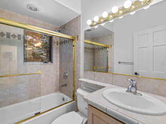 This bathroom features a bathtub with a glass enclosure and a tiled surround, complemented by a decorative tile accent band.
