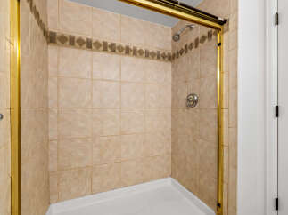 Step into this charming bathroom featuring a tiled shower with a decorative accent band and a sleek gold frame.