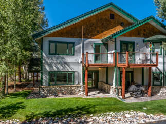 This charming multi-level home features a striking stone foundation and light gray siding, complemented by dark green trim around the windows and roofline.