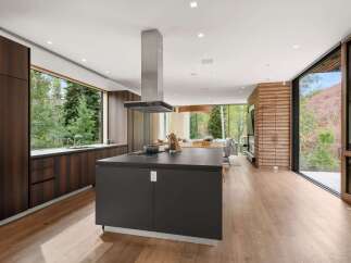 Experience modern luxury in this stunning open-concept kitchen and living area, featuring rich wood cabinetry and a sleek dark island with a gas stovetop.