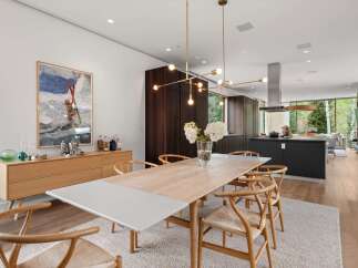 Experience modern luxury in this open-concept dining and kitchen area, featuring a sleek wooden dining table with wishbone chairs and a contemporary brass chandelier.