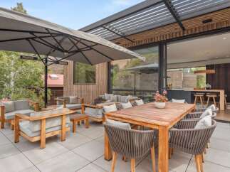 Experience seamless indoor-outdoor living with this expansive patio, featuring a large wooden dining table and comfortable seating areas perfect for entertaining.