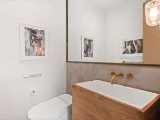 This modern bathroom features a sleek, wall-mounted toilet and a striking wooden vanity with a white basin sink.