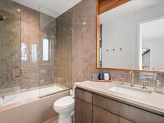 This modern bathroom features a sleek design with taupe subway tile walls and a glass-enclosed bathtub and shower.