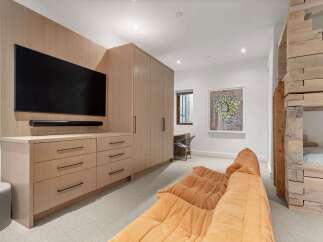 This modern bedroom features a sleek entertainment center with a large flat-screen TV and ample storage, complemented by a cozy orange sectional sofa.