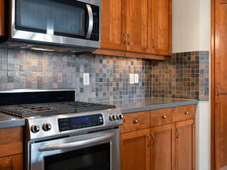 This modern kitchen boasts sleek stainless steel appliances, including a microwave and a gas range, complemented by warm cherry wood cabinetry.