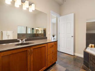 This spacious bathroom features a large vanity with a granite countertop and ample storage, complemented by a tiled bathtub surround.