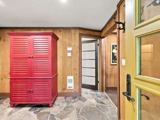 Step into a charming entryway featuring a vibrant red cabinet and rustic wood-paneled walls.
