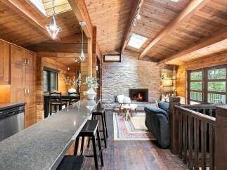 Experience rustic charm in this stunning log cabin featuring a grand stone fireplace and vaulted wood-paneled ceilings with skylights.