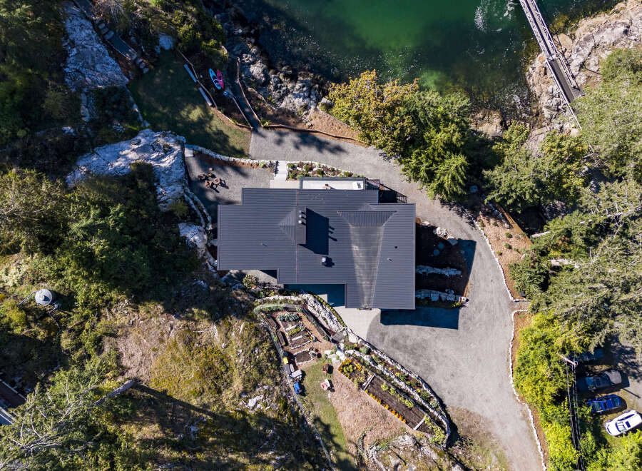 Experience breathtaking waterfront living in this modern home, featuring a sleek dark metal roof and expansive windows.
