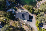Experience breathtaking waterfront living in this modern home, featuring a sleek dark metal roof and expansive windows.