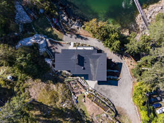 Experience breathtaking waterfront living in this modern home, featuring a sleek dark metal roof and expansive windows.