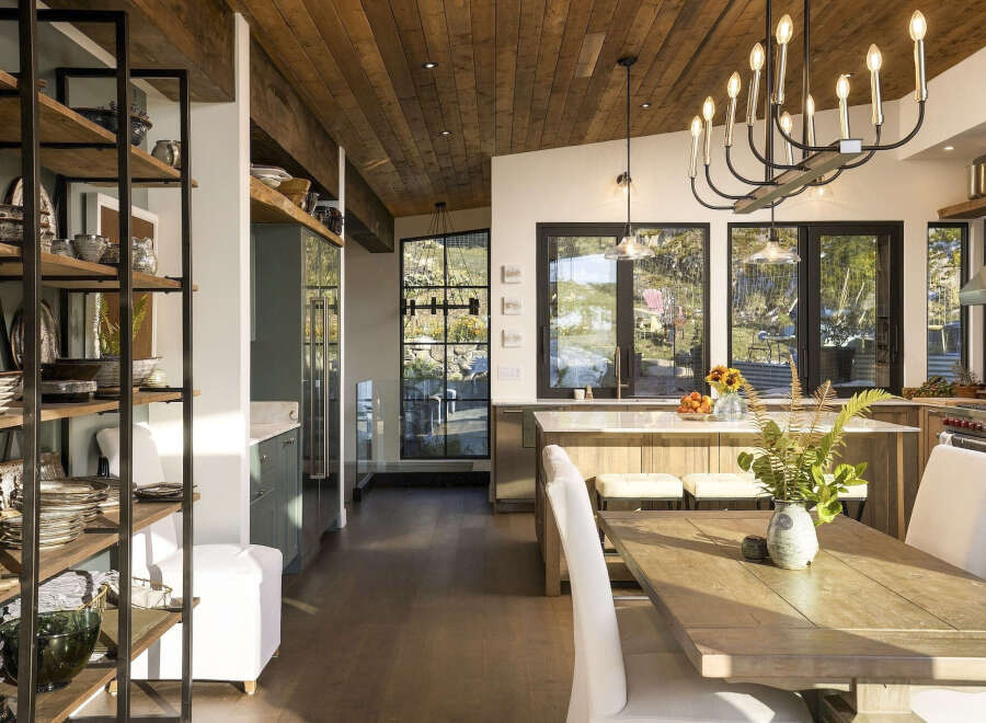 Experience modern rustic charm in this stunning kitchen and dining area, featuring a warm wood-paneled ceiling and expansive windows that flood the space with natural light.