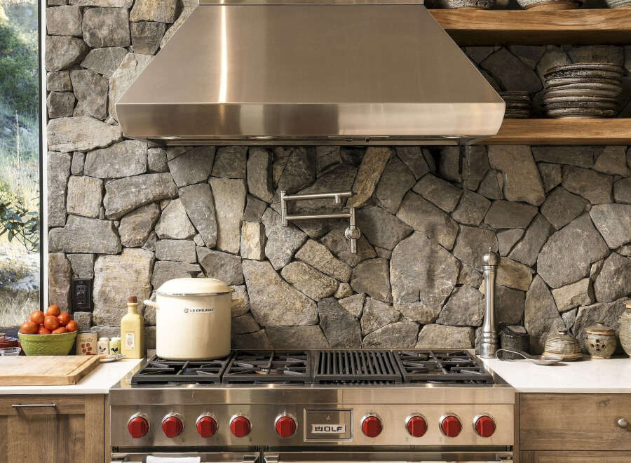 Experience rustic elegance in this stunning kitchen, featuring a dramatic stone accent wall that provides a unique backdrop for the professional-grade Wolf range.