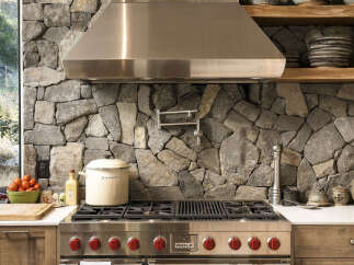 Experience rustic elegance in this stunning kitchen, featuring a dramatic stone accent wall that provides a unique backdrop for the professional-grade Wolf range.