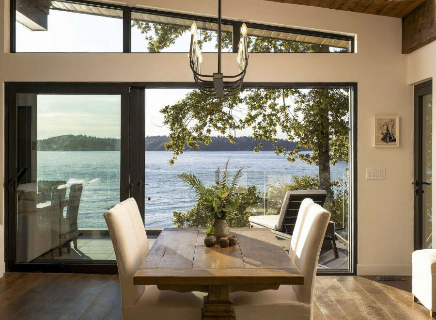 Experience breathtaking waterfront living in this stunning dining area, featuring expansive floor-to-ceiling windows that offer panoramic views of the serene water and lush greenery.