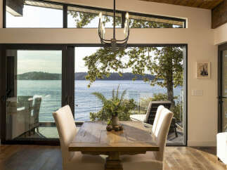 Experience breathtaking waterfront living in this stunning dining area, featuring expansive floor-to-ceiling windows that offer panoramic views of the serene water and lush greenery.