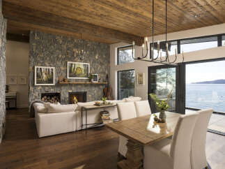 Experience luxurious lakeside living in this stunning home featuring a grand stone fireplace and a rustic wood-paneled ceiling.