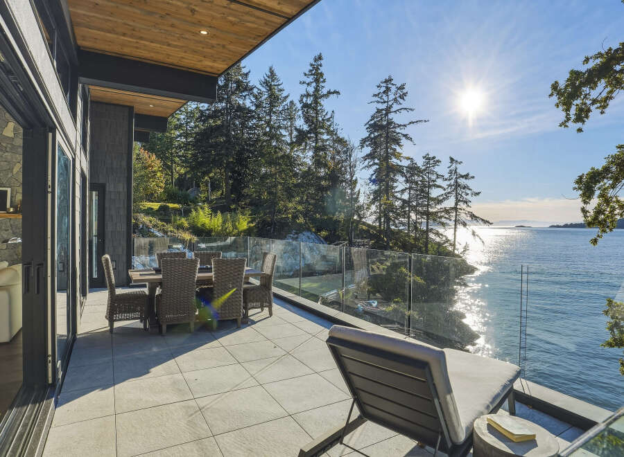 Experience luxurious waterfront living with this stunning patio, featuring a dining set and lounge chair perfect for enjoying the breathtaking ocean views.