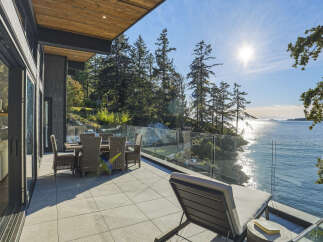Experience luxurious waterfront living with this stunning patio, featuring a dining set and lounge chair perfect for enjoying the breathtaking ocean views.