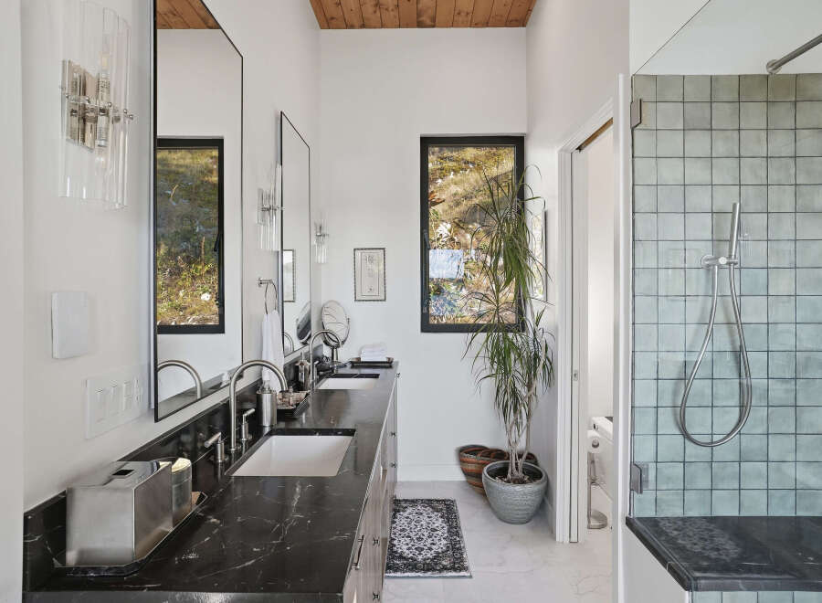 This modern bathroom features a sleek double vanity with a dark marble countertop and undermount sinks, complemented by brushed nickel fixtures.
