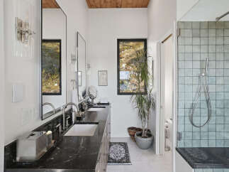 This modern bathroom features a sleek double vanity with a dark marble countertop and undermount sinks, complemented by brushed nickel fixtures.