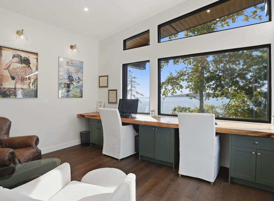 Experience breathtaking waterfront views from this stunning home office, featuring a spacious live-edge desk and comfortable seating.