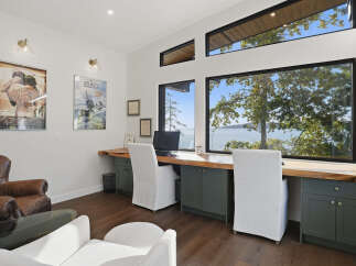 Experience breathtaking waterfront views from this stunning home office, featuring a spacious live-edge desk and comfortable seating.