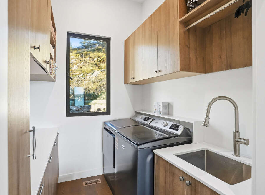 This modern laundry room features a sleek Maytag washer and dryer set, complemented by ample wood cabinetry for storage.