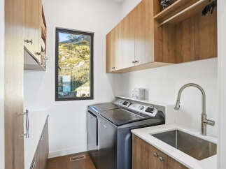 This modern laundry room features a sleek Maytag washer and dryer set, complemented by ample wood cabinetry for storage.