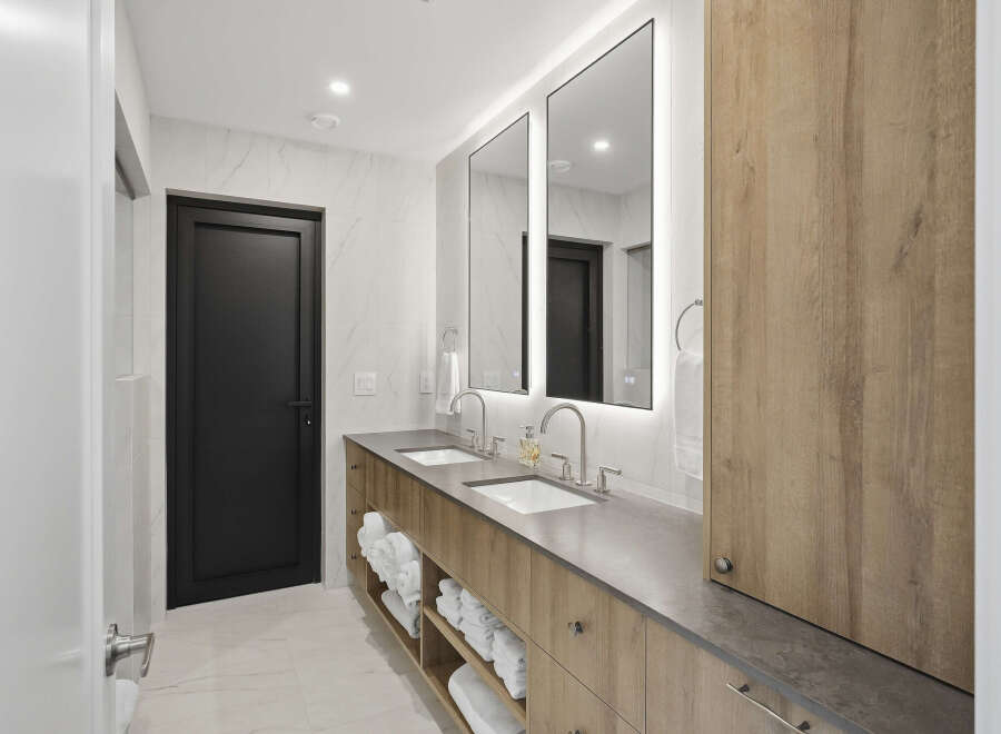 This modern bathroom features a sleek double vanity with a concrete-look countertop and warm wood cabinetry.