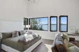 Experience breathtaking ocean views from this luxurious bedroom, featuring a spacious king-size bed adorned with plush pillows and a cozy throw.