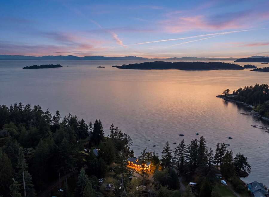 Experience breathtaking sunset views from this stunning coastal property, nestled amidst lush evergreen trees.