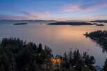 Experience breathtaking sunset views from this stunning coastal property, nestled amidst lush evergreen trees.