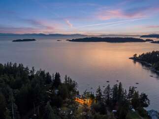 Experience breathtaking sunset views from this stunning coastal property, nestled amidst lush evergreen trees.