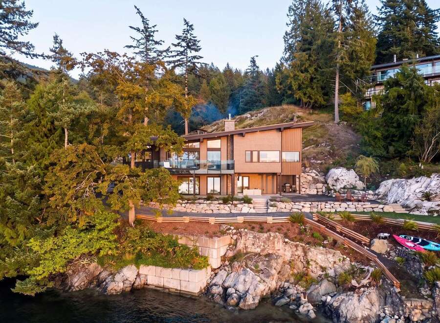 Experience luxury living in this stunning modern home nestled amidst lush trees and rocky shores.