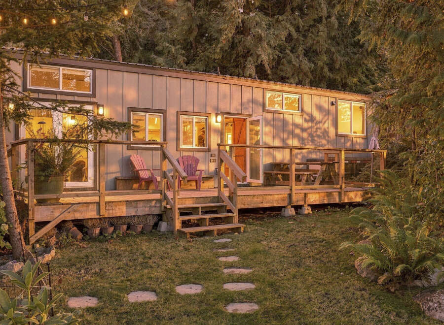 Experience the charm of this cozy tiny home nestled amongst lush trees, bathed in the warm glow of sunset.