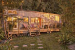 Experience the charm of this cozy tiny home nestled amongst lush trees, bathed in the warm glow of sunset.