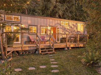 Experience the charm of this cozy tiny home nestled amongst lush trees, bathed in the warm glow of sunset.