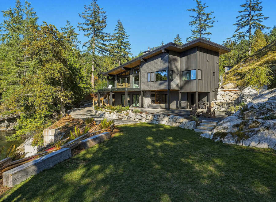 Discover this stunning modern home nestled amidst lush greenery and rocky terrain, offering breathtaking water views.