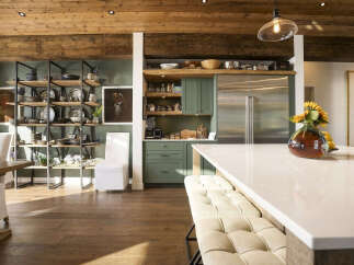 This stunning kitchen boasts a rustic yet modern aesthetic, featuring exposed wooden beams on the ceiling and a sleek, large stainless steel refrigerator.