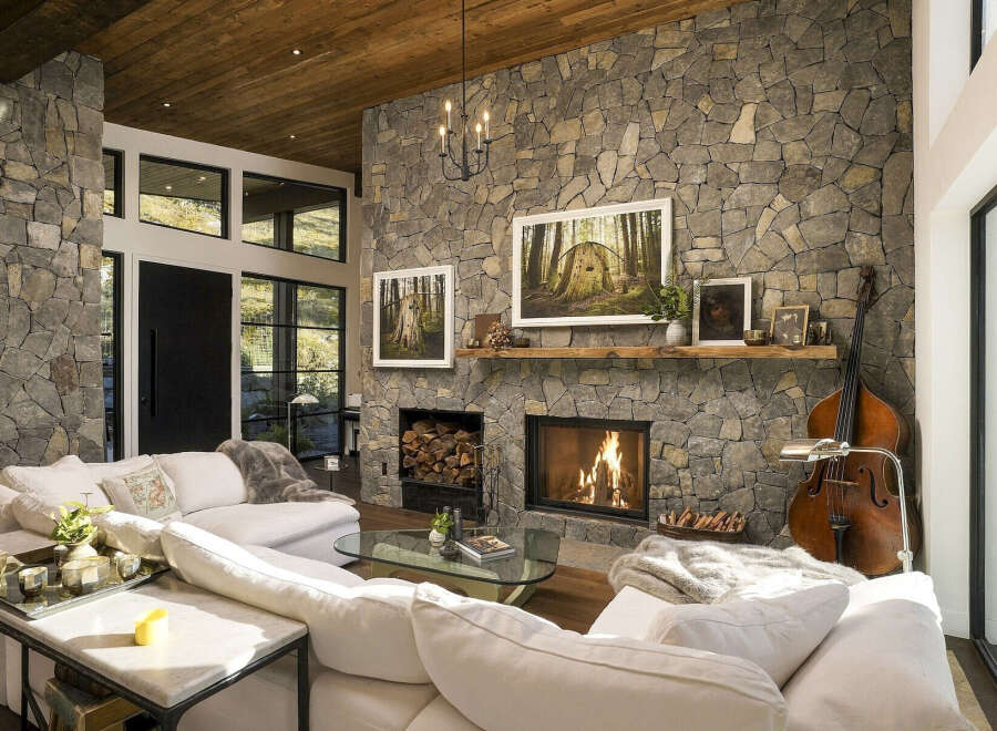 Experience rustic elegance in this stunning living room, featuring a grand stone fireplace with a crackling fire and a rustic wooden mantel.