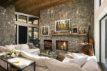 Experience rustic elegance in this stunning living room, featuring a grand stone fireplace with a crackling fire and a rustic wooden mantel.