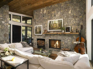Experience rustic elegance in this stunning living room, featuring a grand stone fireplace with a crackling fire and a rustic wooden mantel.