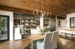 This spacious dining room boasts a rustic wooden ceiling and a modern chandelier, creating a warm and inviting atmosphere.