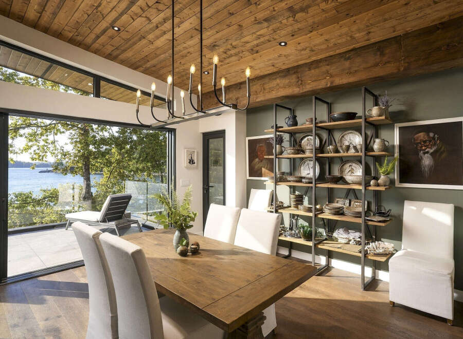 Experience luxurious waterfront living in this stunning dining room, featuring a rustic wooden table and chairs complemented by a modern black chandelier.