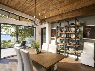 Experience luxurious waterfront living in this stunning dining room, featuring a rustic wooden table and chairs complemented by a modern black chandelier.