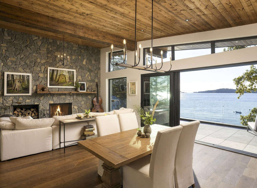Experience breathtaking ocean views from this stunning living and dining area, featuring a grand stone fireplace and a rustic wood-paneled ceiling.