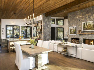 Experience rustic luxury in this open-concept living space, featuring a gourmet kitchen with a large island and a cozy living area centered around a grand stone fireplace.